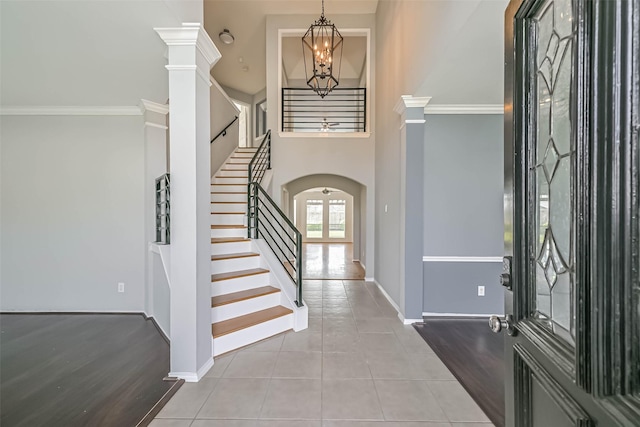 foyer featuring stairway, tile patterned floors, arched walkways, baseboards, and a notable chandelier