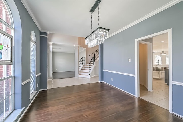 unfurnished dining area featuring stairway, ornate columns, wood finished floors, and ornamental molding