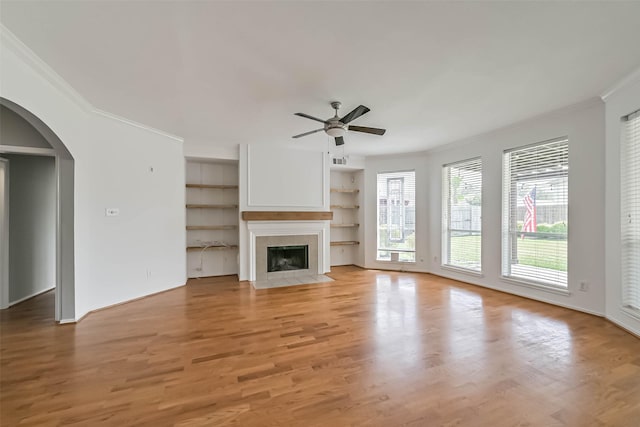 unfurnished living room featuring a ceiling fan, crown molding, arched walkways, light wood-style flooring, and a fireplace