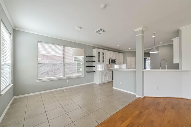 unfurnished living room with baseboards, visible vents, a sink, and ornamental molding