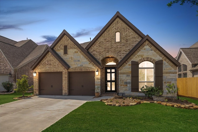 french country inspired facade with a lawn, stone siding, concrete driveway, and brick siding