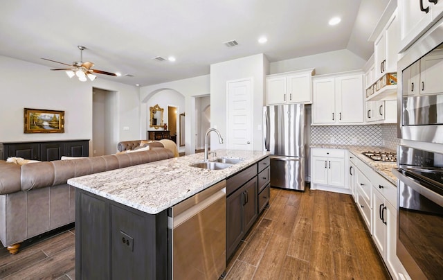 kitchen featuring dark wood-style flooring, open floor plan, arched walkways, a sink, and appliances with stainless steel finishes