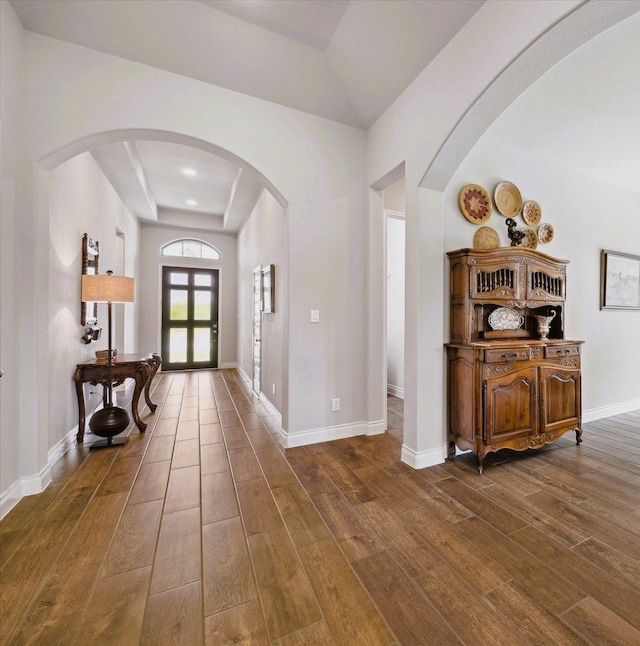 entryway with dark wood-style flooring, arched walkways, french doors, baseboards, and a tray ceiling