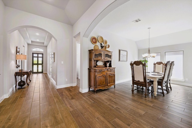 dining room with visible vents, dark wood-style flooring, lofted ceiling, arched walkways, and a notable chandelier