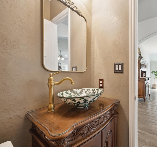 interior space featuring vanity, a textured wall, ceiling fan, and wood finished floors
