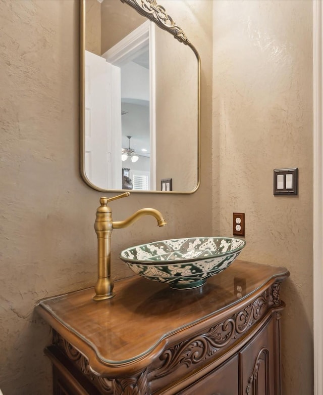 interior details featuring vanity, a ceiling fan, and a textured wall