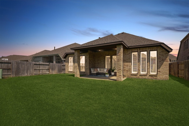 rear view of property featuring brick siding, an outdoor living space, a lawn, and a fenced backyard