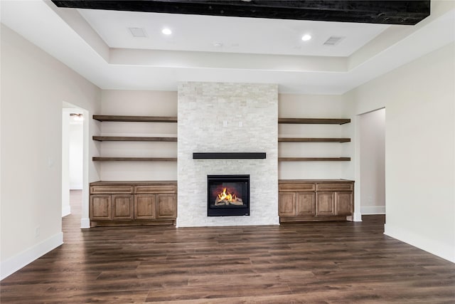 unfurnished living room featuring dark wood-style floors, baseboards, recessed lighting, a stone fireplace, and a raised ceiling