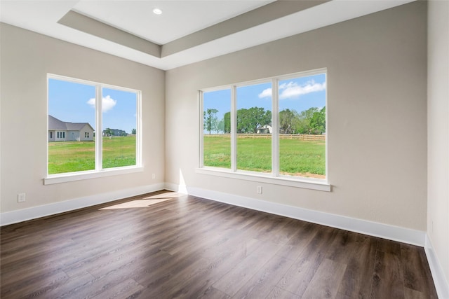 empty room featuring a tray ceiling, baseboards, and dark wood finished floors