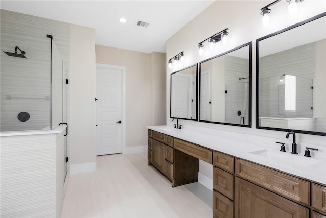 bathroom featuring a sink, double vanity, a tile shower, baseboards, and visible vents