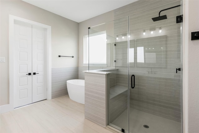 bathroom with tile walls, tile patterned flooring, a freestanding bath, and a stall shower