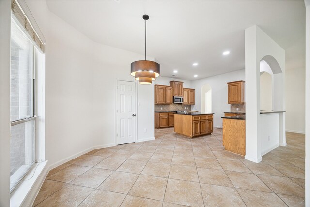 25630 Creston Meadow Dr, Richmond, TX 77406 - kitchen with dark countertops, brown cabinetry, arched walkways, stainless steel microwave, and backsplash