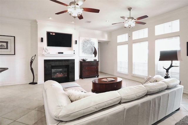 living area featuring light tile patterned floors, ceiling fan, a tiled fireplace, crown molding, and baseboards