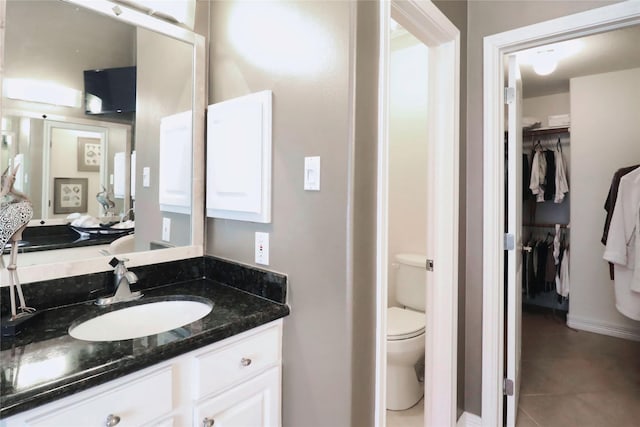 bathroom with tile patterned flooring, toilet, vanity, a spacious closet, and connected bathroom