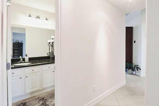 hall featuring light tile patterned floors, baseboards, and a sink