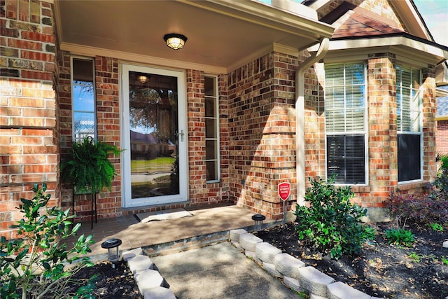 view of exterior entry with brick siding and a porch