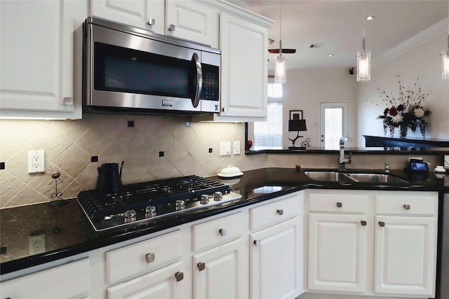 kitchen with stainless steel microwave, gas stovetop, a sink, dark countertops, and white cabinetry