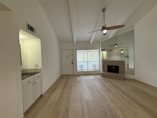 5711 Sugar Hill Dr Unit 62, Houston, TX 77057 - unfurnished living room featuring a fireplace with raised hearth, lofted ceiling with beams, light wood-style floors, ceiling fan, and visible vents