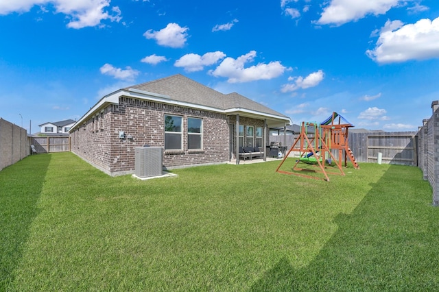 back of house with a playground, a fenced backyard, a yard, central AC, and brick siding