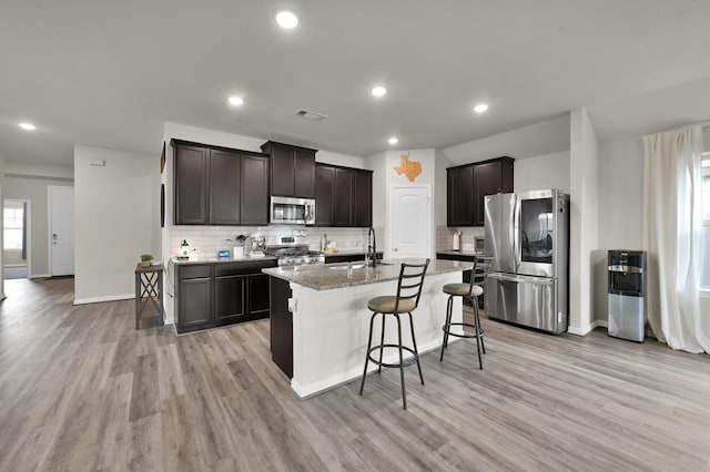 kitchen featuring stainless steel appliances, backsplash, visible vents, light wood-style floors, and light stone countertops