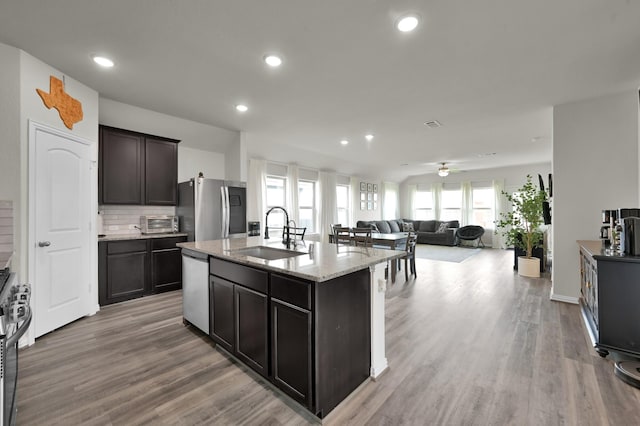 kitchen with light stone counters, light wood-style flooring, stainless steel appliances, and a sink