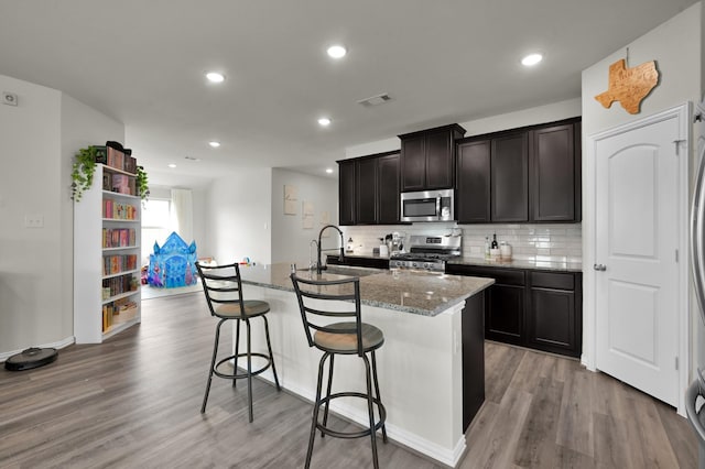 kitchen featuring light stone counters, a breakfast bar, light wood-style flooring, tasteful backsplash, and appliances with stainless steel finishes