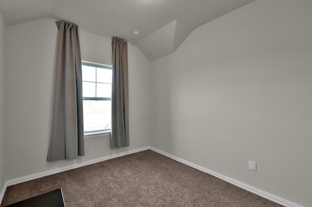 spare room featuring dark carpet, lofted ceiling, and baseboards