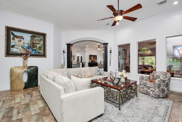 living area featuring arched walkways, visible vents, a ceiling fan, wood finished floors, and ornamental molding