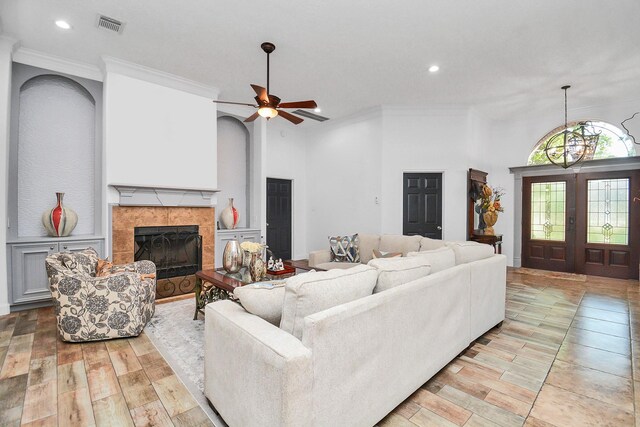 living room featuring a ceiling fan, a tiled fireplace, ornamental molding, visible vents, and recessed lighting