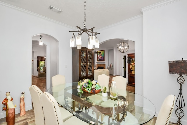 dining area with arched walkways, visible vents, ornamental molding, and an inviting chandelier