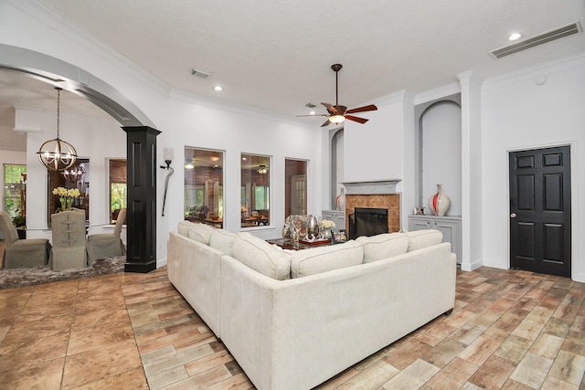 living room featuring arched walkways, visible vents, a glass covered fireplace, ceiling fan with notable chandelier, and ornamental molding