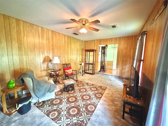 living room with ceiling fan, visible vents, and wooden walls