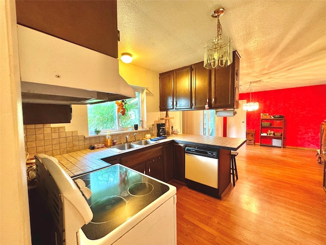 kitchen with ventilation hood, an inviting chandelier, light wood-style floors, white dishwasher, and tile counters