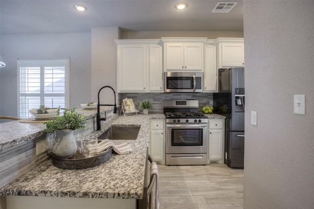 279 Capetown, Conroe, TX 77356 - kitchen featuring appliances with stainless steel finishes, a sink, backsplash, light stone counters, and white cabinets