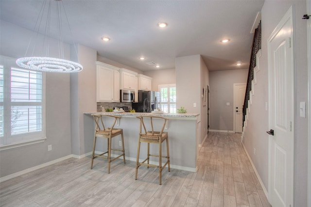 279 Capetown, Conroe, TX 77356 - kitchen with stainless steel appliances, light wood-style flooring, white cabinets, a breakfast bar, and a chandelier