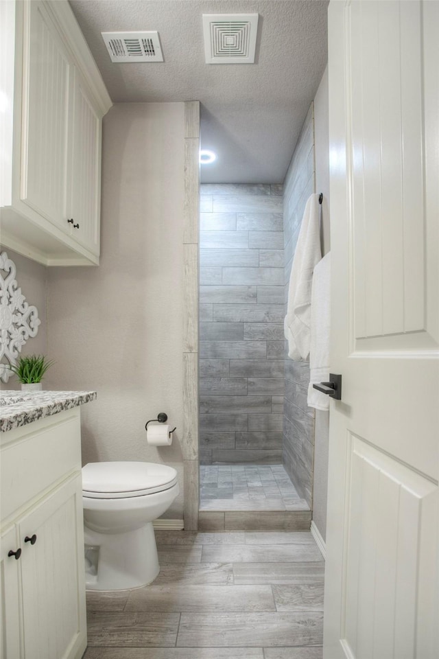 279 Capetown, Conroe, TX 77356 - full bathroom featuring toilet, a tile shower, vanity, wood finished floors, and a textured ceiling