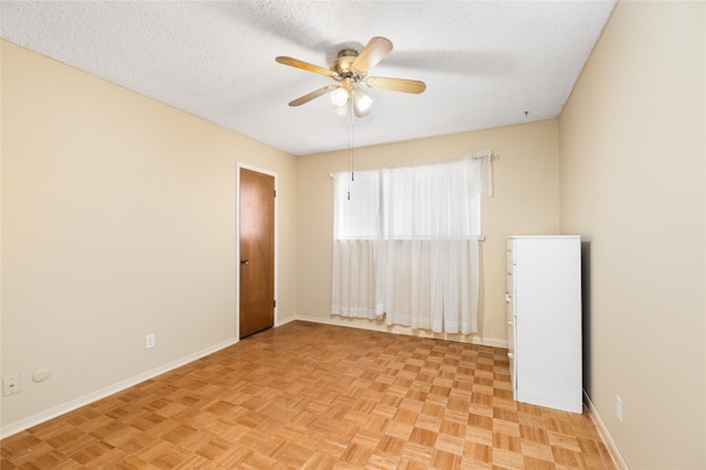 empty room with a textured ceiling, a ceiling fan, and baseboards