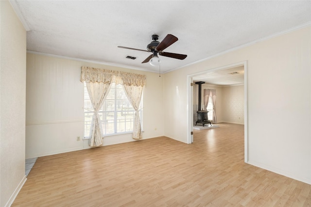 unfurnished room with a ceiling fan, wood finished floors, a wood stove, and crown molding