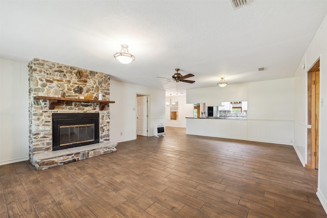 5233 N US Highway 183, Gonzales, TX 78629 - unfurnished living room featuring a stone fireplace, wood finished floors, heating unit, ceiling fan, and visible vents