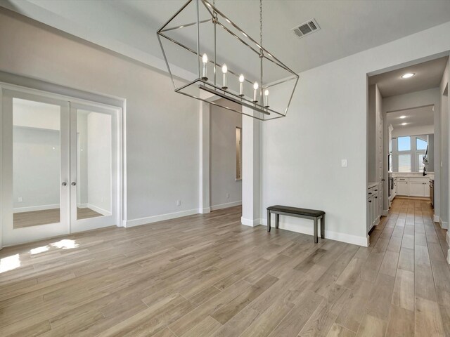 unfurnished dining area with visible vents, light wood-style flooring, french doors, and an inviting chandelier