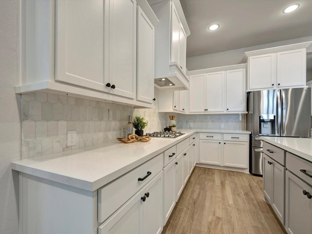 kitchen with wall chimney range hood, backsplash, appliances with stainless steel finishes, light countertops, and light wood-style flooring