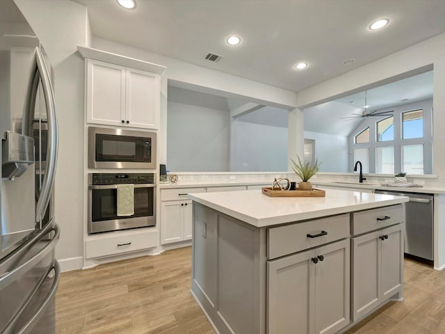 kitchen with a kitchen island, visible vents, light countertops, light wood finished floors, and stainless steel appliances