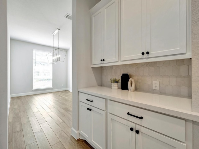 interior space featuring baseboards, light wood-style flooring, backsplash, a notable chandelier, and hanging light fixtures