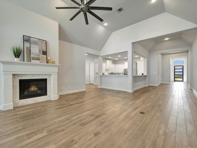 unfurnished living room with visible vents, a glass covered fireplace, light wood-type flooring, a ceiling fan, and vaulted ceiling