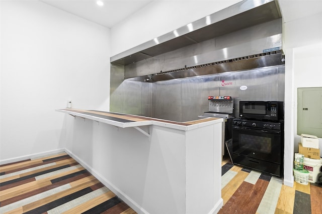 kitchen with wood finished floors, black appliances, electric panel, baseboards, and wall chimney exhaust hood