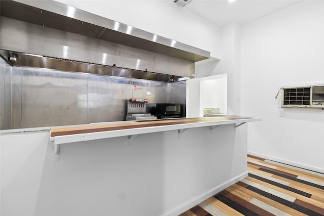 kitchen featuring baseboards, wall chimney exhaust hood, wood finished floors, and a wall unit AC