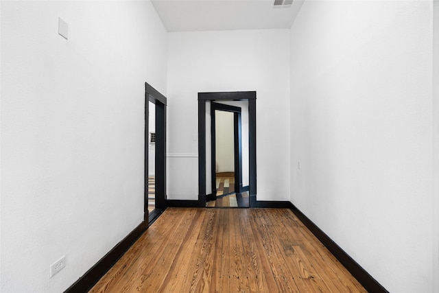 hallway with baseboards, wood finished floors, and visible vents