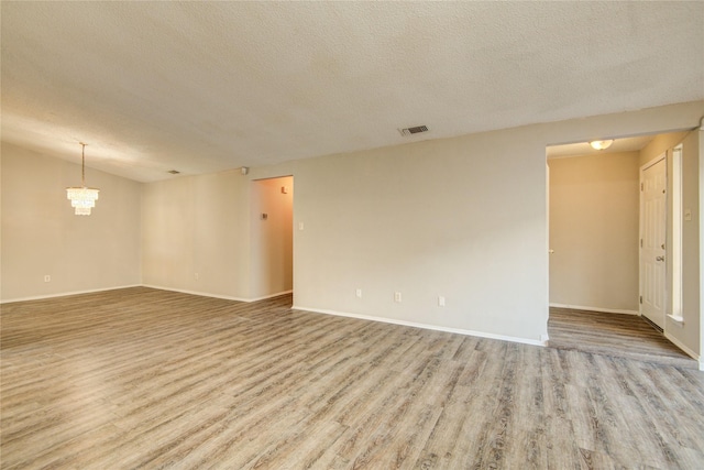 unfurnished room with a notable chandelier, a textured ceiling, visible vents, and wood finished floors