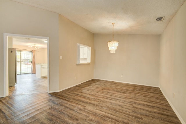 unfurnished room featuring a notable chandelier, baseboards, wood finished floors, and visible vents