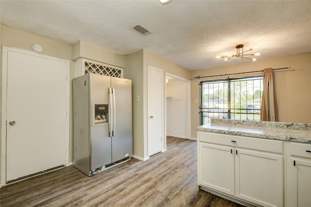 kitchen with wood finished floors, an inviting chandelier, stainless steel fridge with ice dispenser, visible vents, and a textured ceiling